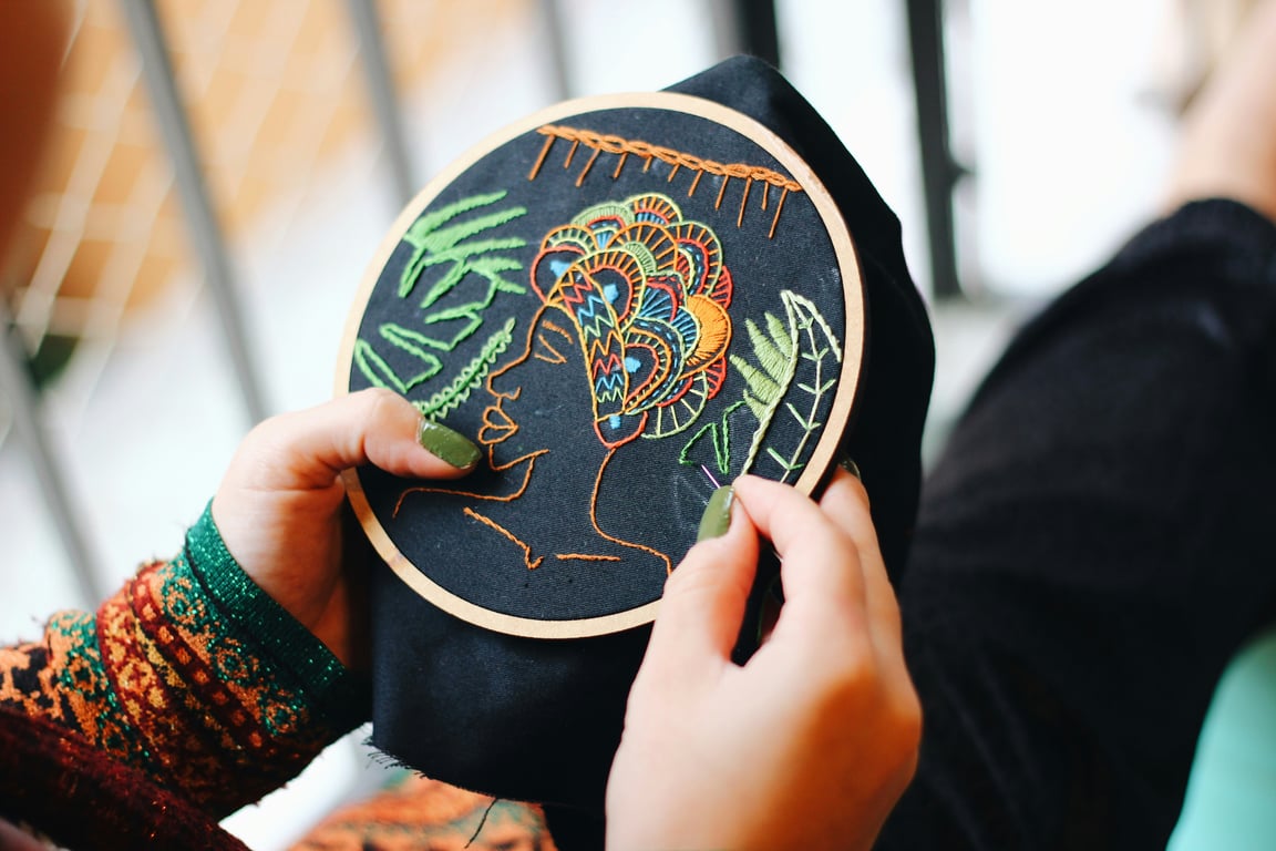 Hands stitching a colourful embroidery design in a wooden hoop